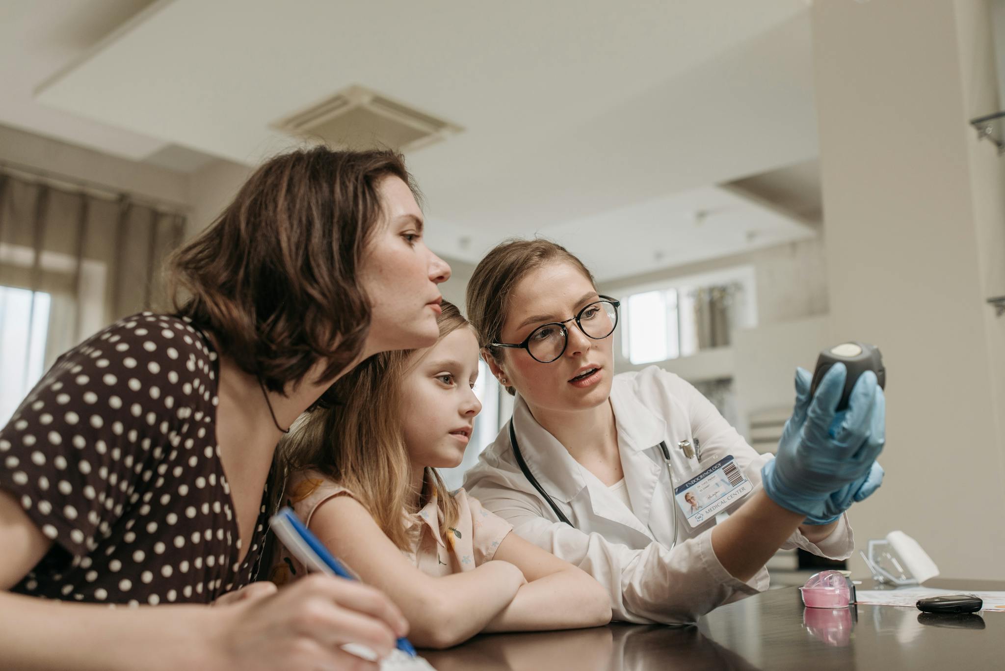 Family doctor explaining a glucometer to a mother and child in a clinic setting indoors.