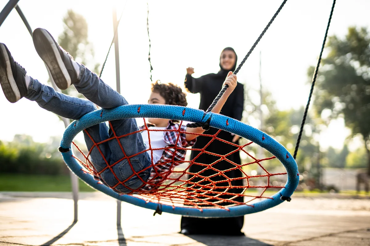 A mother pushing her son on a swing in the park.